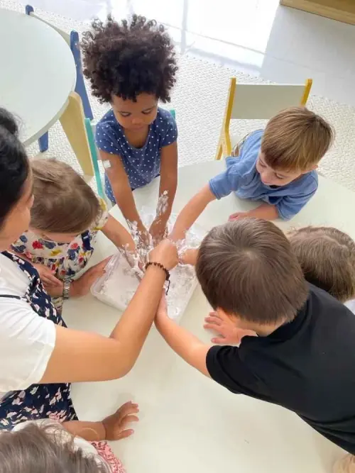 several kids holding mashed white paper with their teacher supervision