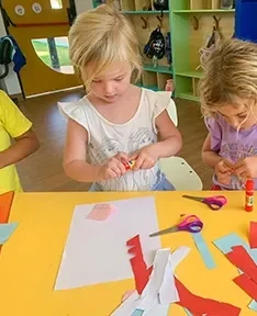 A toddler happily playing with colorful paper, using scissors and glue to create fun crafts.